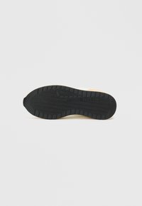 Σόλα παπουτσιού με μαύρη καουτσούκ υφή που διαθέτει σχέδιο κυμάτων, σε αντίθεση με μια ελαφρώς υπερυψωμένη λευκή πλευρά με ελάχιστες σχεδιαστικές λεπτομέρειες.