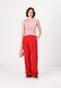 Top senza maniche a righe rosa e bianche, abbinato a pantaloni larghi rossi a vita alta. Gli accessori includono una borsa rosa chiaro e scarpe nere.