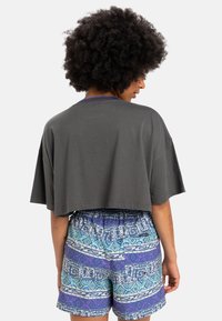 Mørk grå, kortermet t-skjorte kombinert med flerfargede mønstrede shorts med blå, lilla og hvite geometriske design.