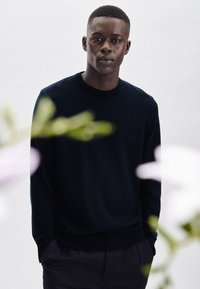 Ciemnogranatowy sweter dzianinowy z okrągłym dekoltem, długimi rękawami i delikatną teksturą, zestawiony z ciemnymi spodniami. Prosty i klasyczny design.