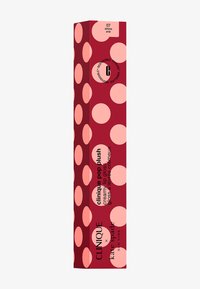 De verpakking van de Clinique Pop Plush lipgloss heeft een dieprode achtergrond met grote roze stippen en zwarte tekst die de kleur "Airkiss Pop" aangeeft.