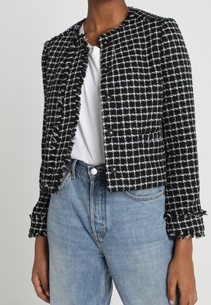 Veste courte à carreaux noirs et blancs avec des bords frangés, portée sur un t-shirt blanc et un jean taille haute bleu clair.