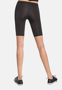Czarne sportowe spodenki kolarskie o gładkiej, elastycznej fakturze, z cięciem sięgającym połowy uda i szerokim elastycznym pasem w talii. Uzupełnione czarnymi sportowymi butami.
