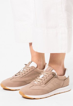 Beige sneaker made of suede with white accents, rounded toe, lace-up design, and side zipper detail. Rubber sole with textured grip.