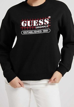 Svart sweatshirt med ett rött rutmönster och en vit "GUESS ORIGINALS ESTABLISHED 1981" logotyp. Ribbad muddar och nederkant.