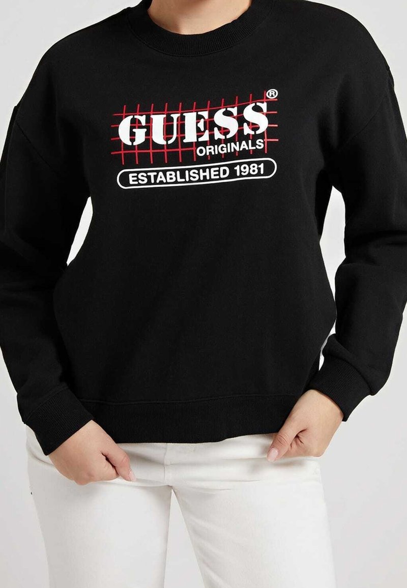 Sudadera negra con un diseño de cuadrícula roja y un logo en blanco que dice "GUESS ORIGINALS ESTABLISHED 1981". Puños y dobladillo acanalados.