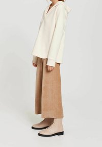 Beige mikina s kapucí, béžové kordové široké kalhoty a světle béžové šněrovací kotníkové boty s černou podrážkou na neutrálním pozadí.