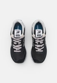 Black New Balance 574 sneakers with a mesh and suede upper, grey laces, and a white rubber sole. Features a padded collar and classic branding.