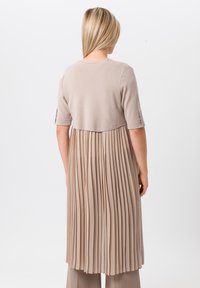 Ensemble beige en deux pièces avec une jupe plissée et fluide et un haut ajusté. Les manches courtes présentent des accents décoratifs au niveau des poignets. Tissu doux et texturé.