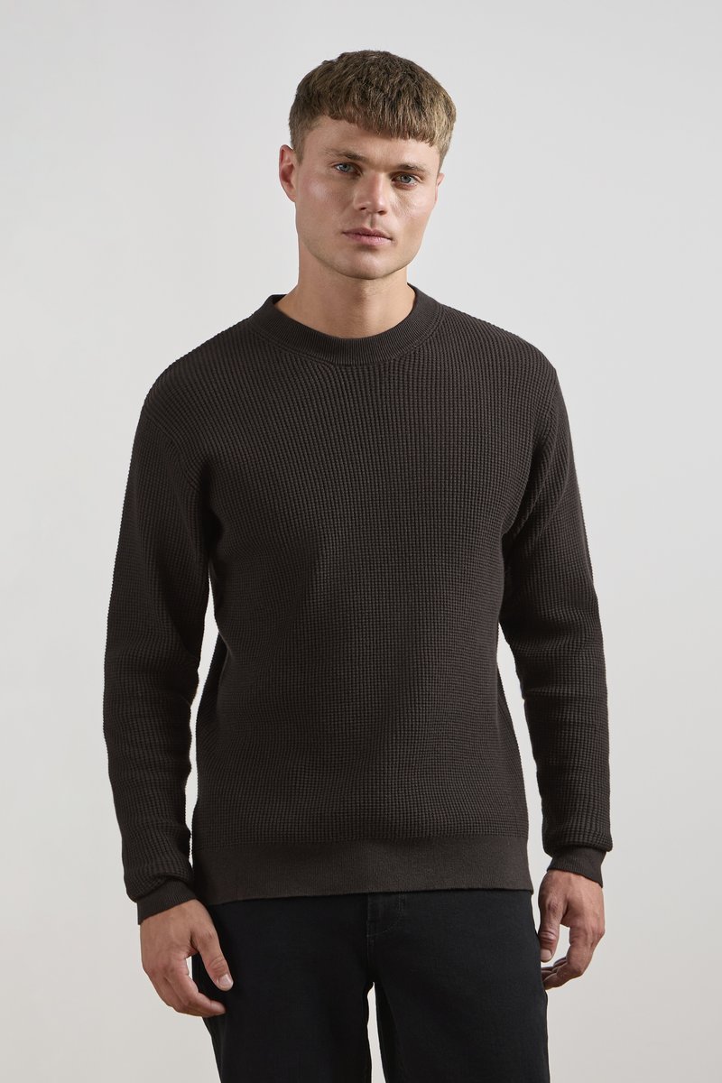 Dark brown ribbed knit sweater with a round neckline, long sleeves, and a ribbed hem. Smooth texture with a fitted silhouette.