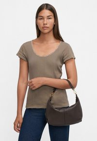 Borsa a tracolla in pelle marrone con forma curva e manico corto, abbinata a un top taupe a coste con scollo rotondo e maniche corte.