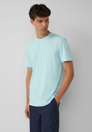 Helles blaues Baumwoll-T-Shirt mit Rundhalsausschnitt und kurzen Ärmeln, das eine glatte Textur und eine taillierte Passform aufweist, kombiniert mit dunkelblauen Shorts.