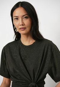 Zwarte T-shirt met een geknoopte voorkant en gespikkelde glitters. Bevat geborduurde details "06 90" op de borst. Korte mouwen, ontspannen pasvorm.