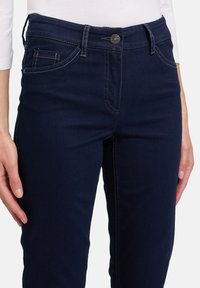 Pantalons en denim bleu marine à coupe classique, avec une fermeture éclair, un bouton de fermeture, des coutures contrastantes et un design de poche avant.