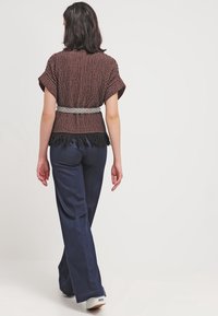 Brunmönstrad topp med korta ärmar, fransad nederkant och ett vitt vävt bälte. Kombinerad med marinblå vida byxor och vita sneakers.