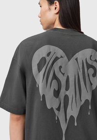 Camiseta extragrande gris oscuro con un gran gráfico de forma de corazón goteante en gris claro en la parte de atrás. Tejido de algodón con una textura suave.
