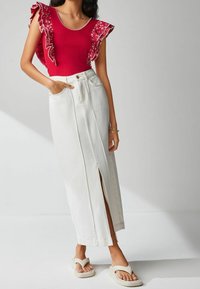 Haut rouge avec des manches à volants fleuris, associé à une jupe maxi en denim blanc avec une fente frontale, et des sandales en plastique beige.
