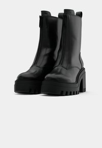 Black mid-calf platform boots with chunky heels, front zippers, and pull tabs on a plain light background.