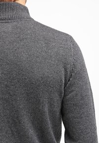 Suéter de punto gris oscuro con un cuello alto, tejido texturizado y un diseño simple, visto desde la parte posterior.