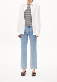 Camisa blanca de botones sobre una camiseta de rayas en blanco y negro, combinada con vaqueros rectos de un tono azul claro y sandalias negras con tacón cuadrado.
