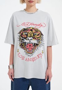 Šedé oversized tričko s barevným grafikou tygra, červenými a zlatými akcenty a textem "Ed Hardy Los Angeles" v tučném písmu.