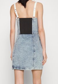 Jeansklänning med åtsittande bodice, vita justerbara axelband, svart bakpanel och ljusblåtvättad, urtvättad look. Har enkel sömnad och rak fåll.