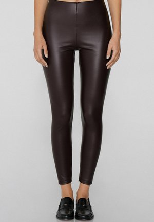 Leggings de imitación cuero marrón con un ajuste slim, cintura alta y textura suave. Llevados con mocasines negros, mostrando una silueta elegante.