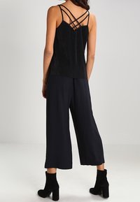 Top in tessuto nero con design a incrocio delle bretelle sul retro, abbinato a pantaloni neri a gamba larga e stivali neri alla caviglia.