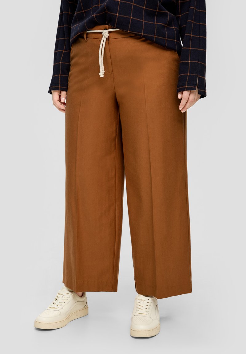 Pantalones marrones de pierna ancha con cintura ajustable, hechos de una tela suave, combinados con zapatillas beige y una camiseta de manga larga a cuadros en color marino.
