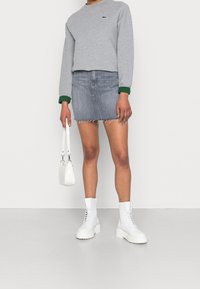 Grå sweatshirt med gröna manschetter, blå denimkjol med fransad nederkant, vita snörkängor och en liten vit handväska.