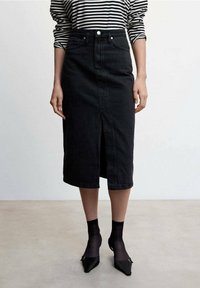 Jupe crayon en denim noir avec une fente avant, des boutons en métal et un design à cinq poches. Associée avec un haut à rayures noir et blanc.