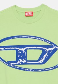 T-shirt de algodão verde com um grande design gráfico em azul e branco. Decote redondo com acabamento em ribana, textura suave e detalhe de logótipo em destaque.