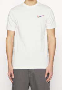 Vit bomullströja med korta ärmar, som har en flerfärgad Nike-logotyp på vänster bröst. Slät textur, normal passform.
