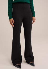 Melnas izplūdušas bikses ar augstu jostu, ar vertikālām šuvēm. Audums ir gluds ar nelielu spīdumu. Apvienotas ar arādas melniem zābakiem.