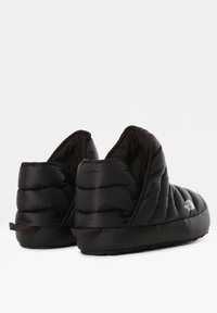 Zapatillas aislantes negras con textura acolchada, espalda alta y suela de goma. Presentan un pequeño logo en el lado exterior.