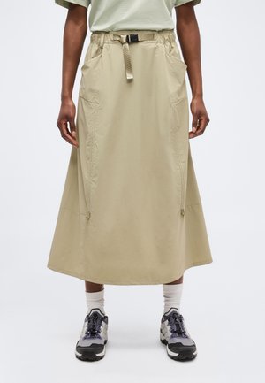 Beež midi seelik, millel on reguleeritav vöö ja küljetaskud, kantud valgete sokkide ning helel taustal hallide ja mustade matkajalatsitega.