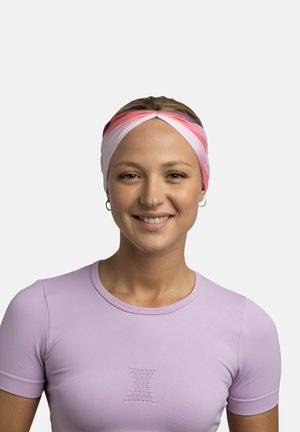 Young woman smiling, wearing a pink, white, and purple headband and a light purple short-sleeve top against a plain light background.