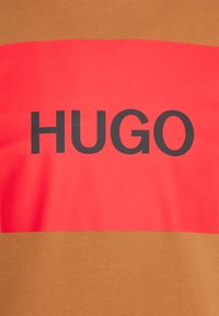 Brown and red T-shirt with horizontal color blocks. "HUGO" printed in black on the red section. Smooth fabric, regular fit, minimal texture.