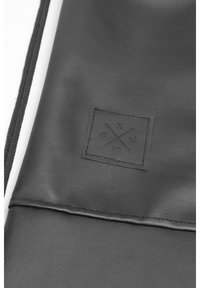 Schwarze Lederhandtasche mit einer strukturierten Oberfläche, genähtem Rand und einem quadratischen Logopatch mit verschiedenen Symbolen in der Mitte.