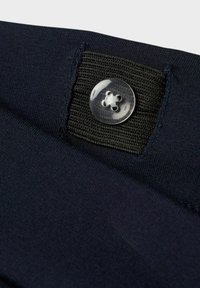 Tissu bleu marine avec une texture lisse et une bande élastique noire visible ornée de détails en bouton transparent, positionnée sur le bord supérieur.