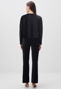 Schwarzes, strukturiertes Zweiteiler-Outfit mit einem kurzes, langärmliges Oberteil und weit geschnittenen Hosen, von hinten präsentiert.