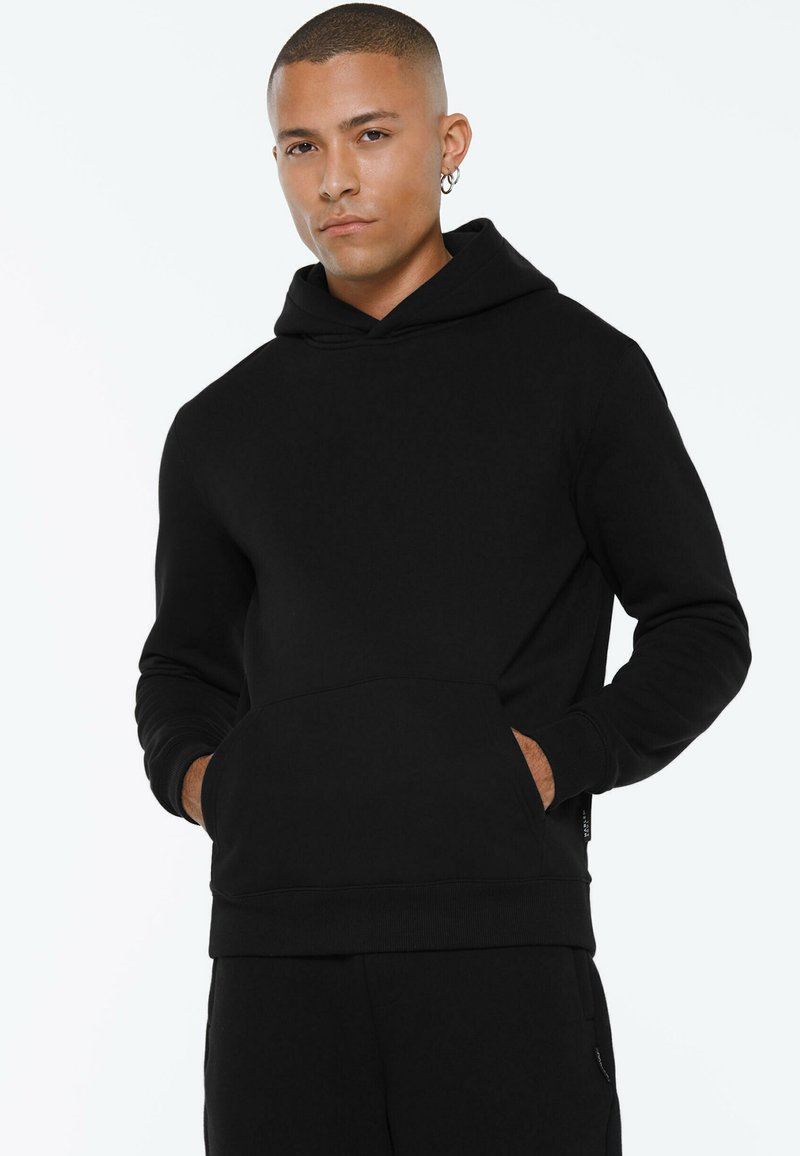 Black hoodie made of soft fabric, featuring a front kangaroo pocket, ribbed cuffs, and a drawstring hood. Simple, modern design.