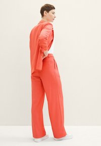 Coral blazer and wide-leg pants in lightweight fabric, featuring a relaxed fit. Model paired with white sneakers. Simple, solid design.