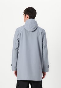 Vandtæt grå frakke med hætte, justerbare ærmer og en afslappet pasform. Stoffet ser glat ud med en mat finish.