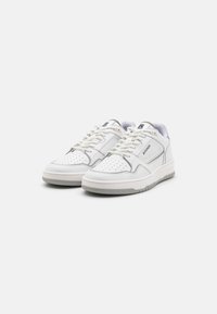 White sneakers with a textured leather upper, perforated detailing, grey accents, round toe, and flat rubber sole. Brand logo on the side.