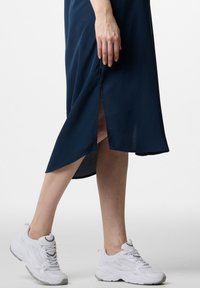 Marineblaue Midikleid mit einem seitlichen Schlitz, gefertigt aus einem glatten Stoff. Kombiniert mit weißen Sportsneakern mit einer strukturierten Sohle.