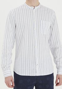 Camisa de algodón de botones en blanco con rayas verticales azules. Presenta un cuello mao y un bolsillo en el pecho. Mangas largas con puños abotonados.