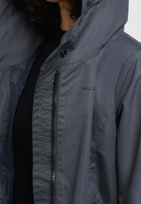 Graue wasserdichte Jacke mit einem Reißverschluss, knöpfbarem Kragen und Logodetail. Verfügt über eine glatte Textur und eine Kapuze für zusätzlichen Schutz.