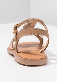 Sandalia de cuero marrón con múltiples correas delgadas y un tobillo con hebilla, que presenta una plantilla de textura suave y una suela plana y flexible.