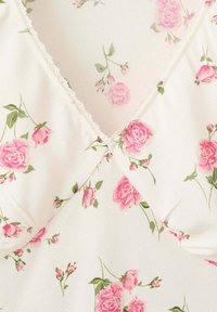 Tissu blanc avec motif floral de roses roses et feuilles vertes, avec un col en V bordé d'une délicate bordure en dentelle blanche.